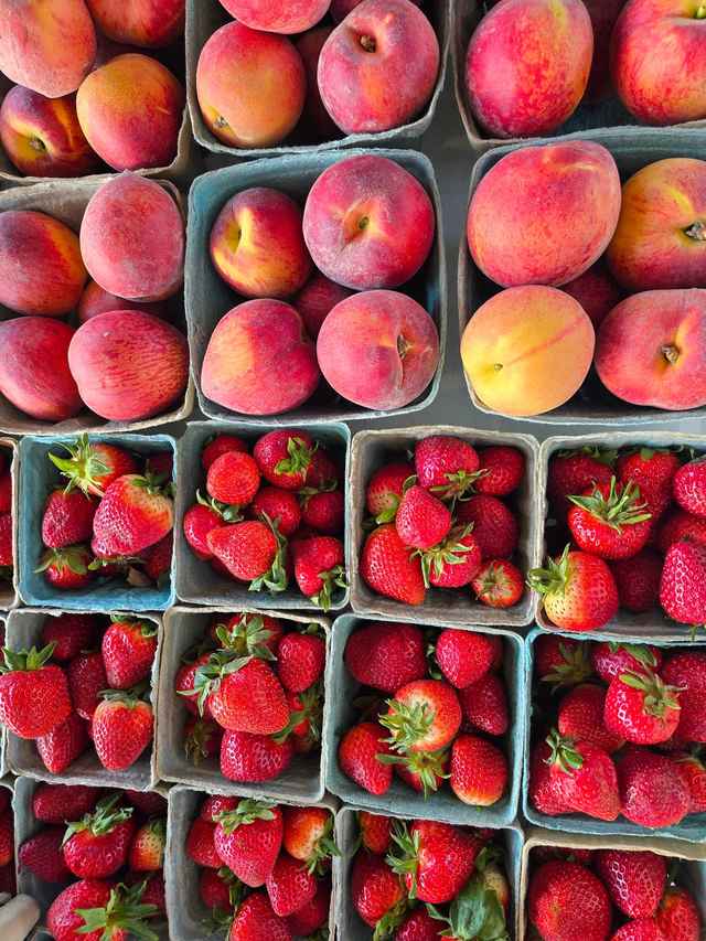 Baskets of ripe peaches above quarts of fresh strawberries